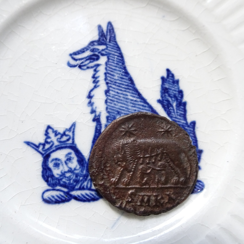 Wolf and Head Saucer: ironstone with underglaze blue printed decoration. Lying on top is a Roman bronze coin showing the wolf suckling Romulus and Remus, with the inscription 'SMKA' indicating the Carthage mint.