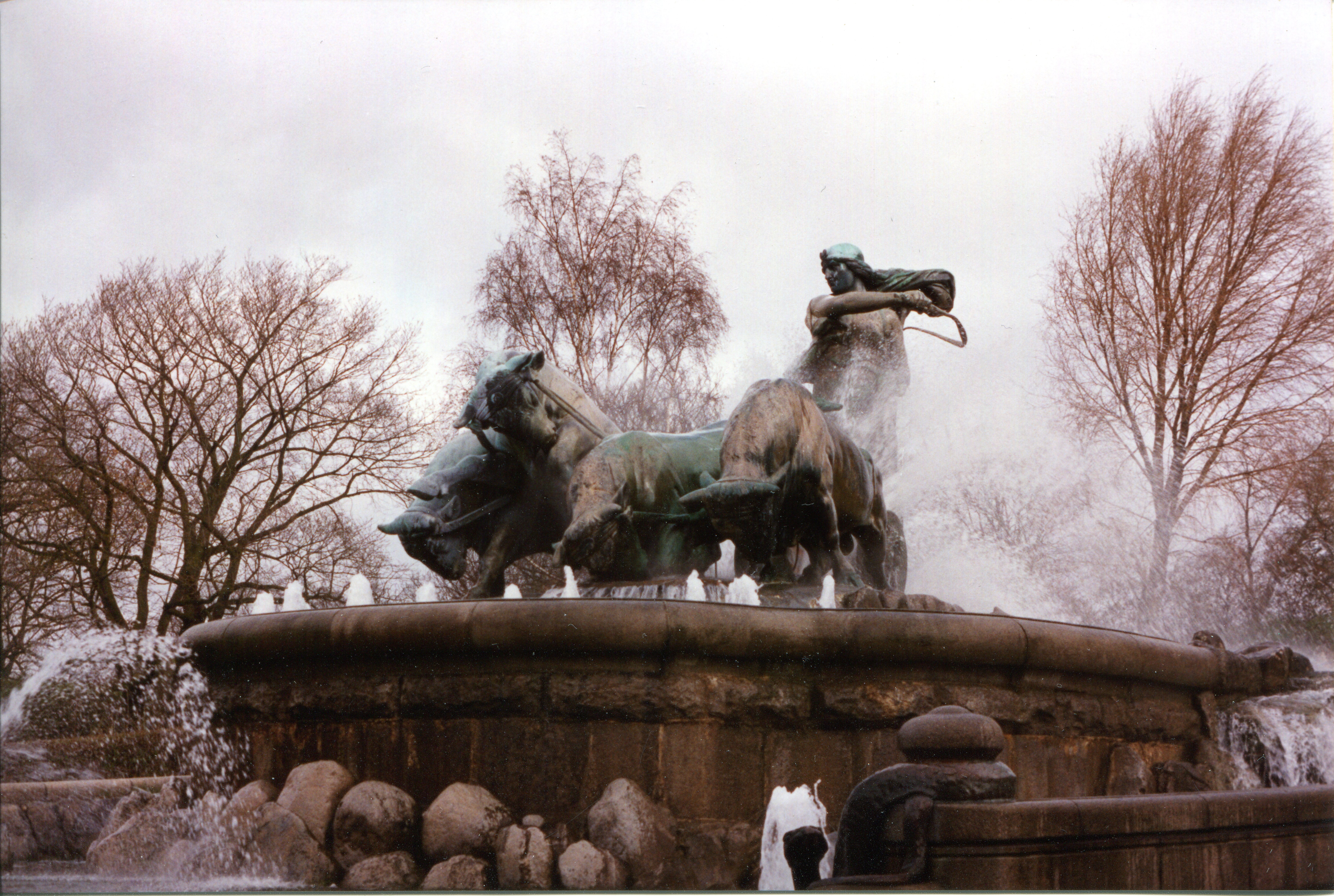 A large fountain, surrounded by water spray, in which Gefjon ploughs with four oxen, flailing a whip in her right hand. One of the oxen is rearing to the side.