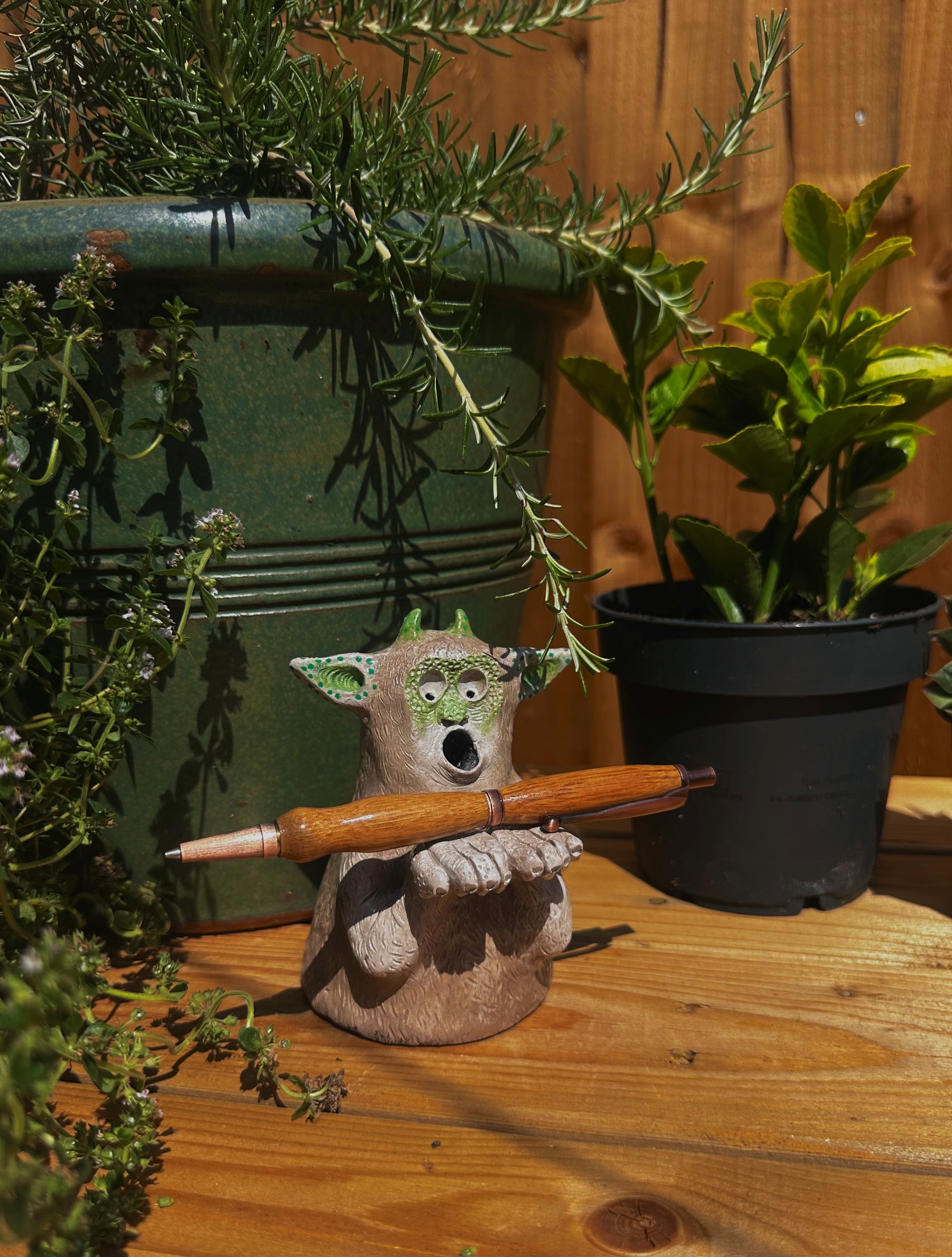 A ceramic creature with gaping mouth holding a pen in front of a pot of rosemary. Picture by Jodie Hyson.