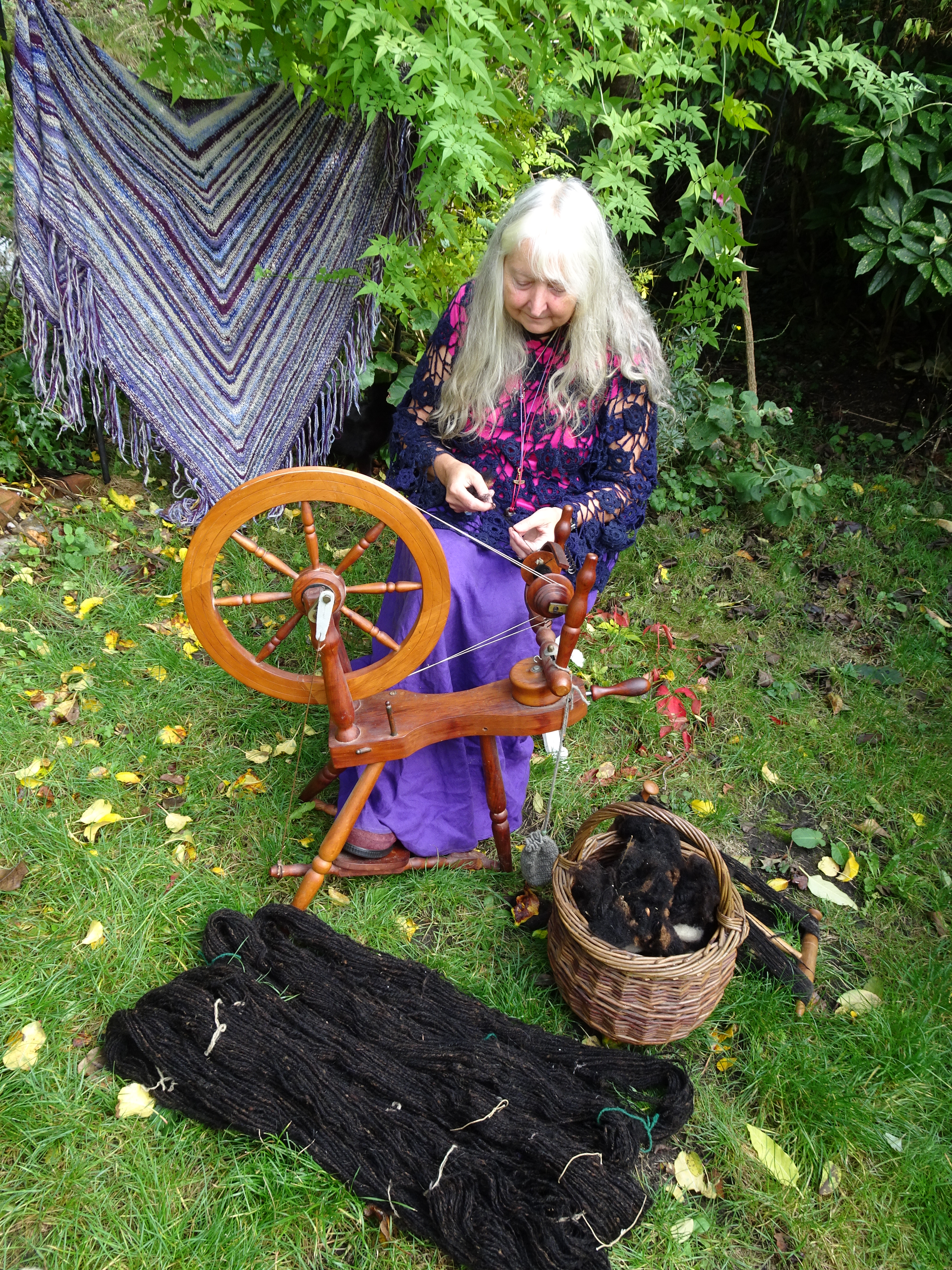 Image promoting the Norwich Moot on-line spin-in for St Catherine's Day, showing Val Thomas spinning in a garden.